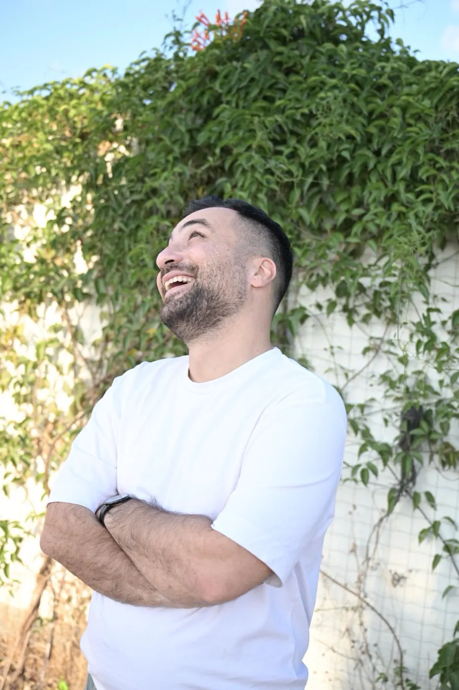 ניב צוחק, ידיים שלובות, מול קיר קיסוס